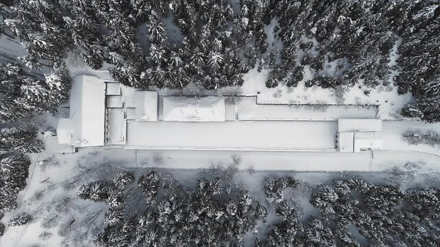 Aerial winter view of snowy isolated building complex in the middle of forest. Drone front view of snowy and desolated landscape in a winter journey 
