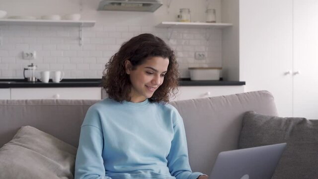 Happy hispanic teen girl holding laptop computer device technology sitting on couch at home. Smiling young woman using apps, searching online, e learning, studying browsing internet on sofa.