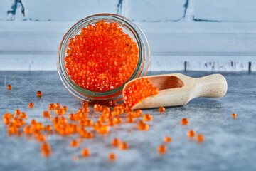 A jar of red caviar and wooden spoon on marble background