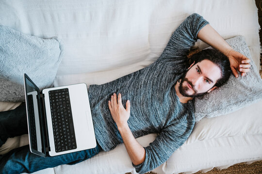 Man with laptop lying on sofa at home