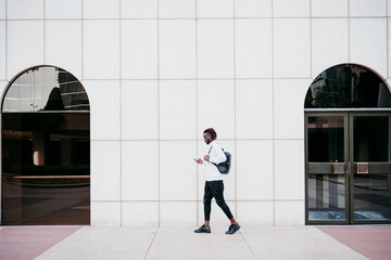 Young man using mobile phone while walking by wall in city