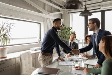 Diverse business partners shaking hand in modern boardroom after negotiation, signing contract,...