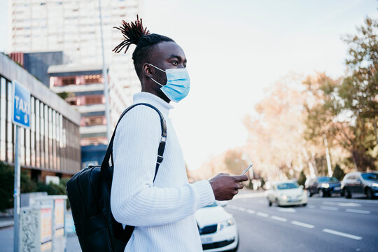 Young man with mobile phone on city street during COVID-19