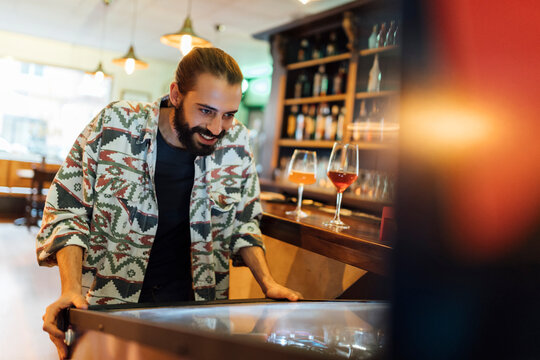 Bearded man playing pinball in bar
