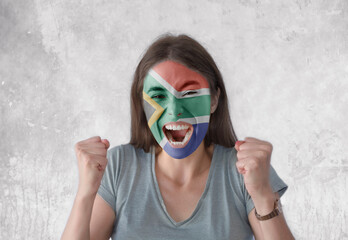Young woman with painted flag of South Africa and open mouth looking energetic with fists up
