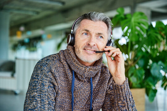 Mature businessman smiling while talking on headset sitting at office
