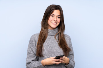 Teenager Brazilian girl over isolated blue background sending a message with the mobile