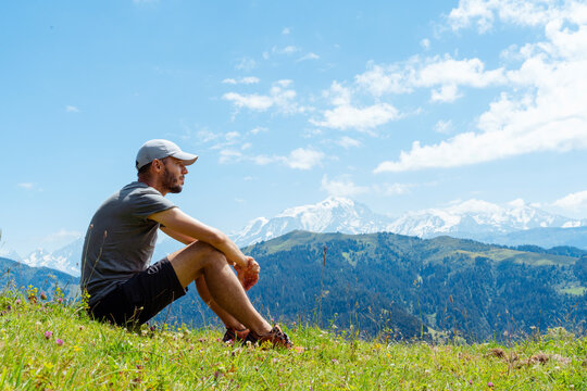 Mid adult man contemplating while sitting over grass at at Col des Aravis, Haute-Savoie, France