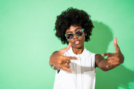 Woman wearing sunglasses gesturing while standing against green background