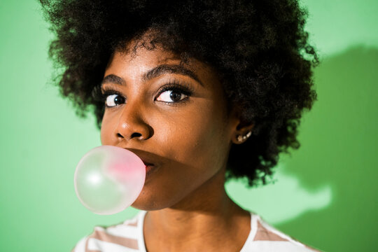 Young woman blowing bubble gum while standing against green background