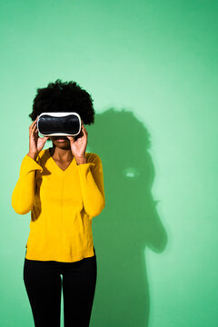 Young woman using virtual reality headset while standing against green background