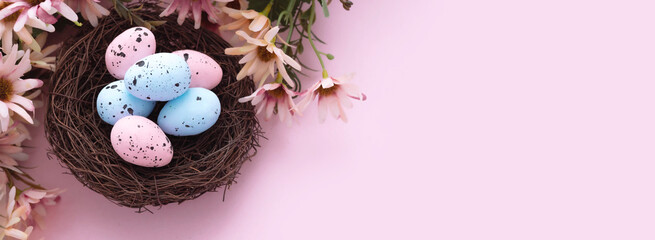 Obraz na płótnie Canvas Colorful easter eggs in nest and flowers on pink background with copy space. Flat lay. Banner