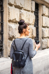 Fototapeta na wymiar Back view of a young woman with a hot drink and backpack walks in a European city