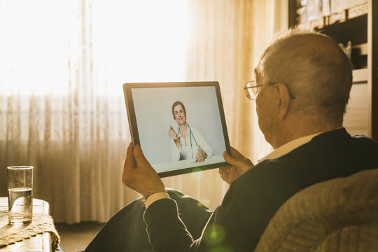 Female doctor showing medicine to male patient on video call over digital tablet in living room