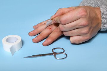 A man's hand, a finger with a cut, wound, bruise, glues itself an adhesive plaster. First aid antiseptic, protection against bacteria.