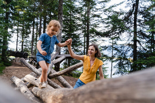 Mother assisting little daughter walking on top of wooden logs