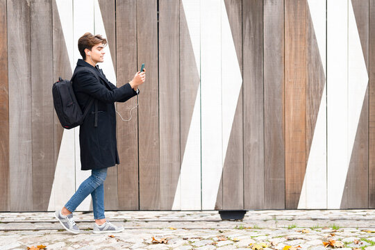Young man with backpack walking while on video call by wall