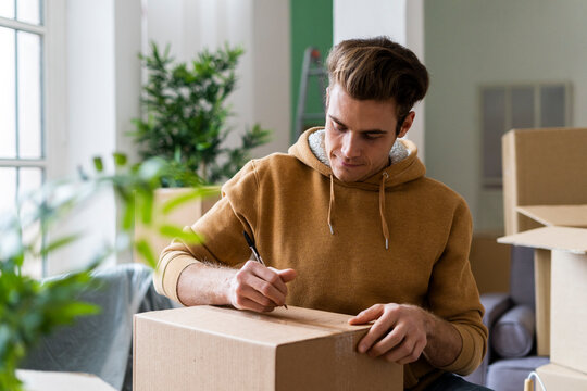 Young man writing on cardboard box with pen in new home