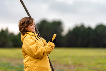 Portrait of young boy standing outdoors with branch and smart phone in hands