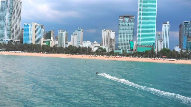 Aerial view of the city beach and active people practicing kite surfing and windsurfing. Kitesurfing place, sports concept, healthy lifestyle, human flight.