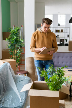 Young man holding list while standing by box with plant in new loft apartment