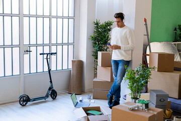 Young man using mobile phone while listening music by leaning on column in new home