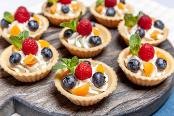 Fruit and berry tartlets dessert assorted on wooden tray. Closeup of delicious pastry sweets pies colorful cakes with fresh natural raspberry blueberry and cheese cream. French bakery catering.