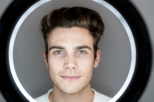 Young male influencer seen through circle light against gray background