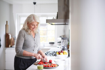 Retired woman cutting strawberries on board in kitchen at home