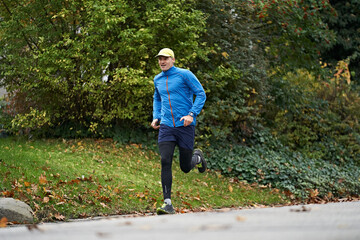 Mature man in sports clothing running on footpath by grass