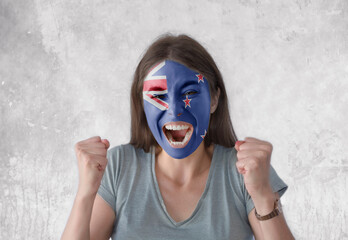 Young woman with painted flag of New Zealand and open mouth looking energetic with fists up