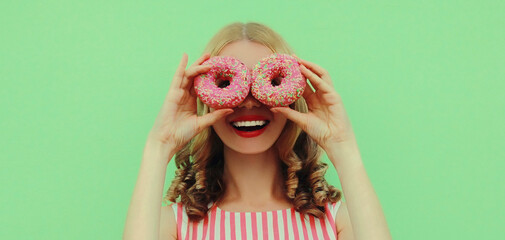 Portrait close up of happy smiling young woman with two donuts having fun on a green background