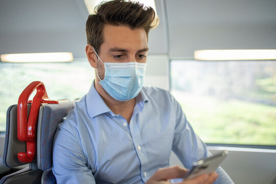 Businessman wearing face mask using smart phone while sitting in train