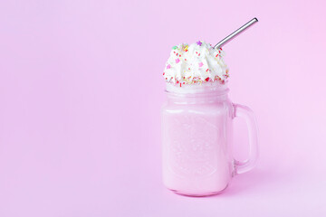 Pink milkshake with cream and sprinkles on pink background