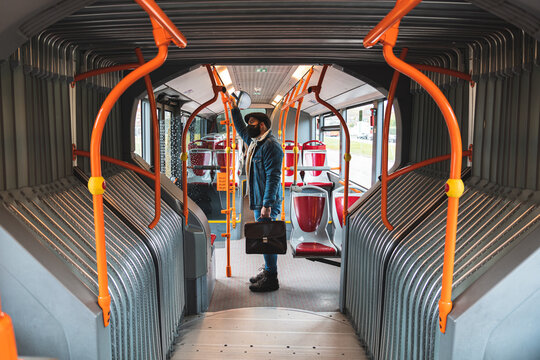 Commuter with briefcase holding pole while standing in bus during COVID-19
