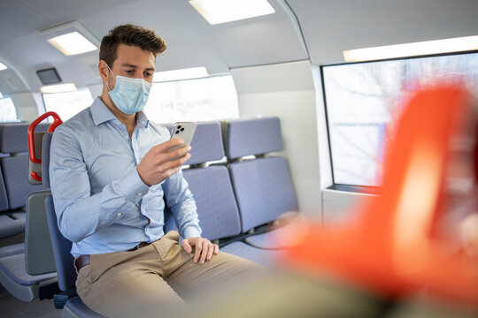 Businessman wearing protective face mask using mobile phone while sitting in train