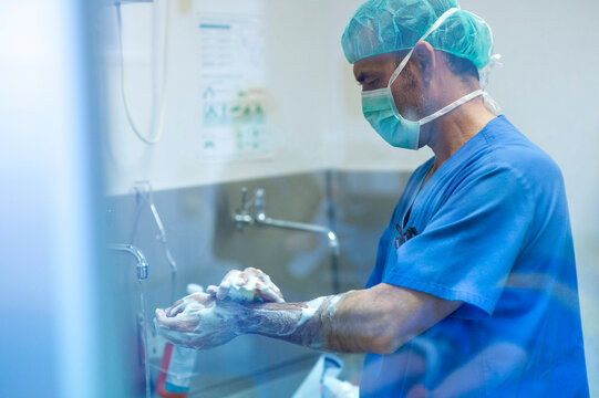 Male orthopedic surgeon washing hand with soap by sink in hospital