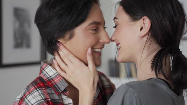 Two happy young affectionate women lesbian lgbtq couple dating lauhging at home together, kissing passionately, hugging enjoying intimate tender sensual moment, bonding in apartment. Lgbt love concept