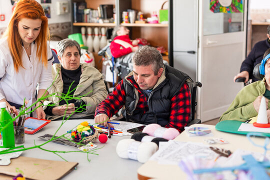 Female nurse doing creative craft with disabled man and woman in nursing home