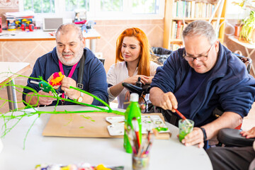 Mature disabled men doing art and craft with female caregiver at rehabilitation center