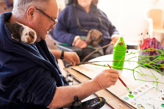 Mature disabled man painting twig at rehabilitation center