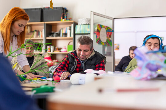 Redhead female caregiver doing creative craft with disabled man and woman in nursing home