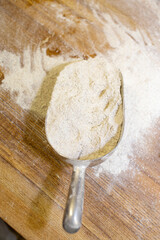 Wheat flour on a wooden table and a measuring spoon.