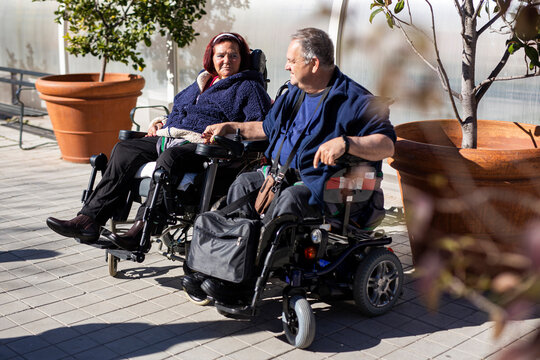 Disabled woman and man holding hands while sitting on wheelchair during sunny day