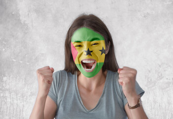 Young woman with painted flag of Sao Tome and Principe and open mouth looking energetic with fists...