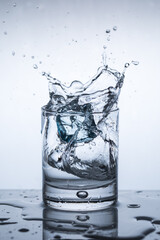 Splash of ice in a glass of water, an ice cube falls into a glass of water, close up