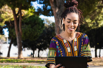 Beautiful Jamaican woman with dreadlocks using digital tablet at park on sunny day