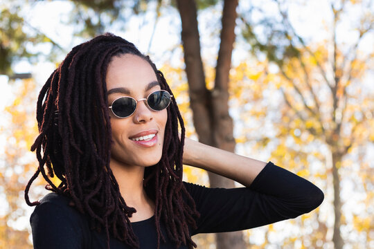 Fashionable young woman with dreadlocks wearing sunglasses at park