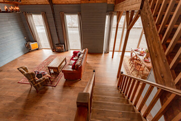 cozy all wooden interior of a country house in a wooden design. spacious living room with kitchen area with large windows. bedroom on the second floor.