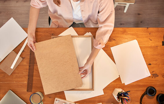 Female artist holding wooden picture frame at desk while working at home